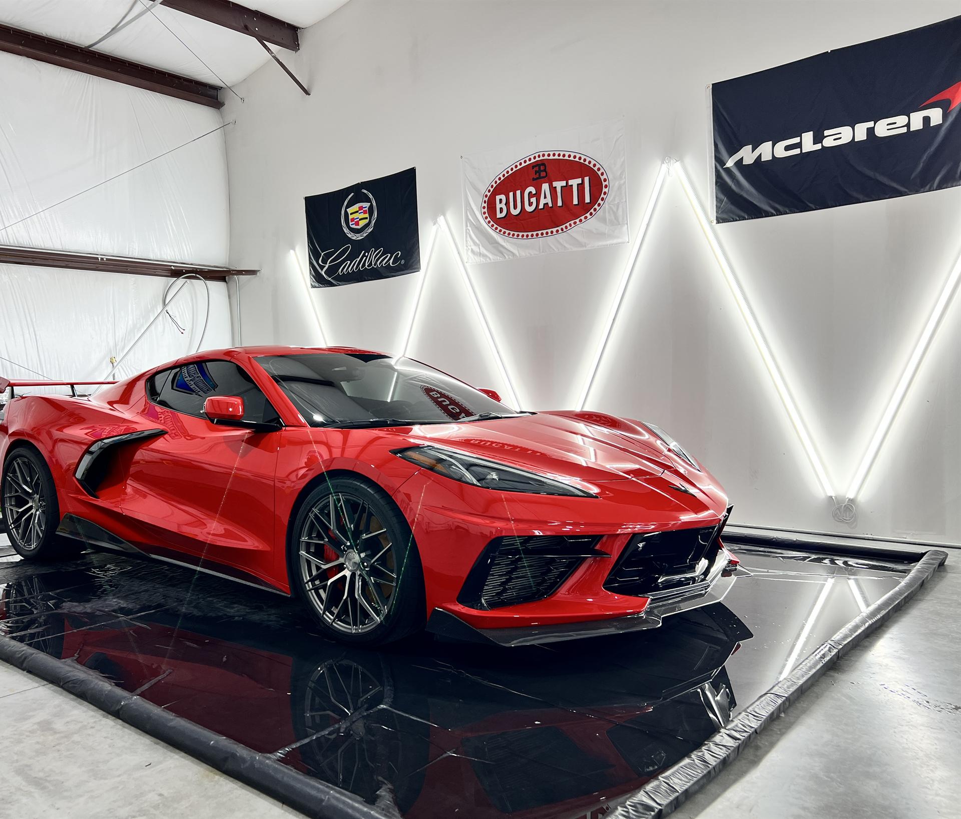 Red Chevrolet Corvette C8 detailed and staged under accent lighting inside the Glowtek Auto Care shop in Cypress, Texas